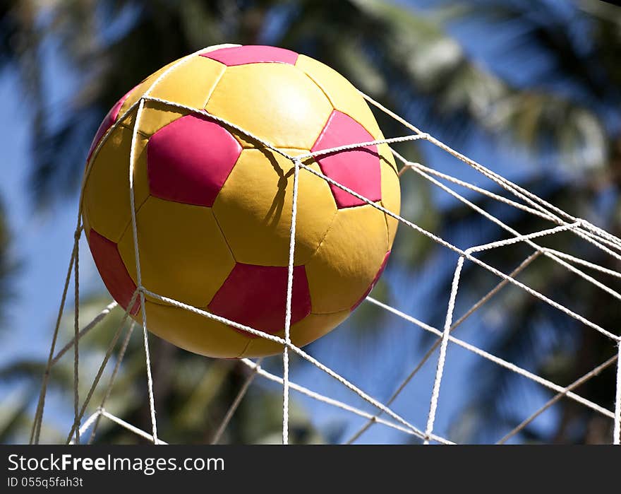 The soccer ball in the net gate on the background of blue sky and palm trees. The soccer ball in the net gate on the background of blue sky and palm trees