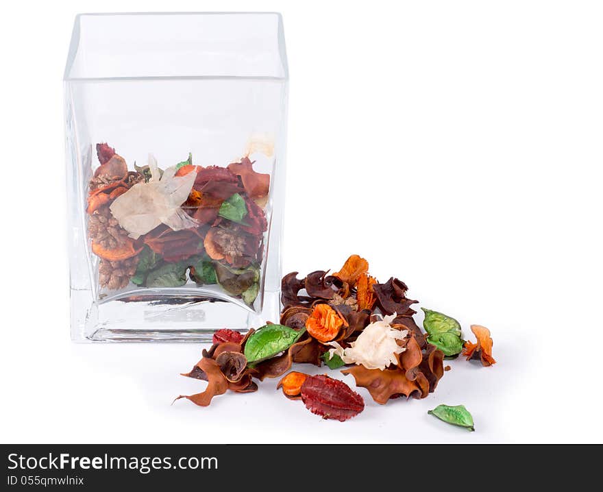 Colorful natural pot pourri with dried seasonal flowers, leaves and spices on a white background alongside a half full glass container for a scented fragrance in the house