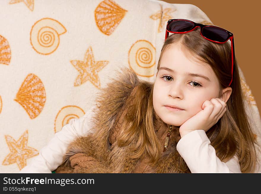 Young attractive blonde girl with sunglasses on her head and wearing a fluffy waistcoat relaxing in front of a cushion covered in fabric patterned with seahsells. Young attractive blonde girl with sunglasses on her head and wearing a fluffy waistcoat relaxing in front of a cushion covered in fabric patterned with seahsells