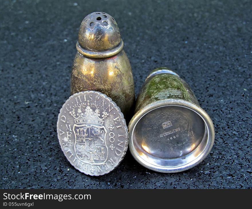 Antique silver salt and pepper shakers and an old Spanish coin on a black background. Antique silver salt and pepper shakers and an old Spanish coin on a black background.