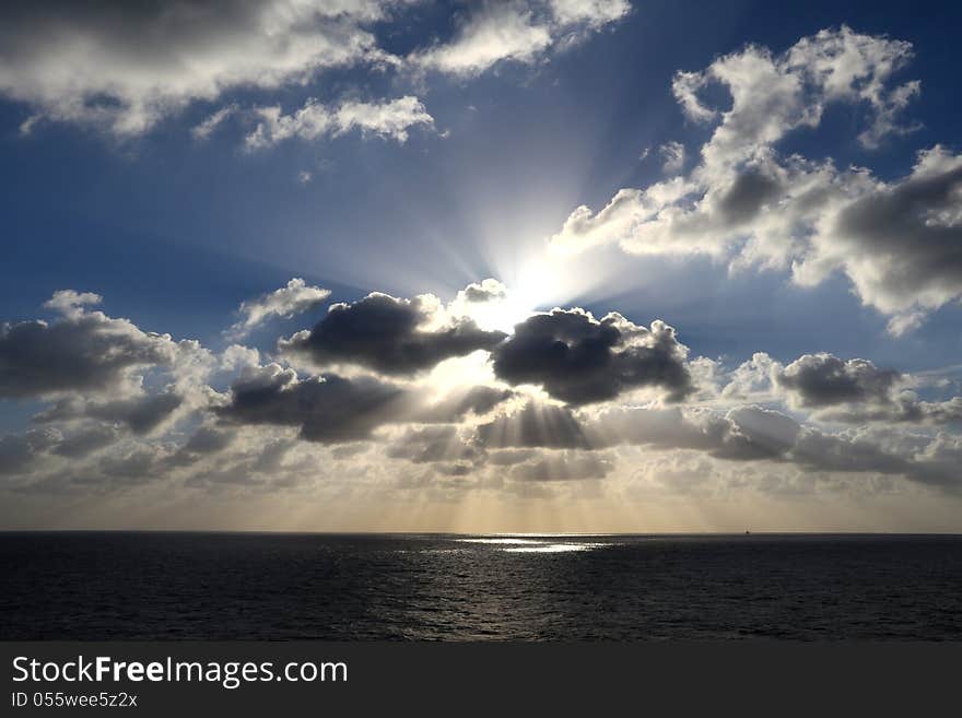 Light rays shine through the group of clouds in the middle of the ocean