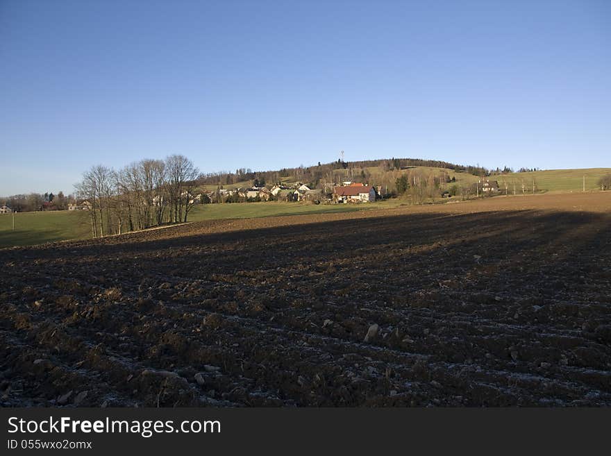 Plowed field in the shadow in the background with the village. Plowed field in the shadow in the background with the village