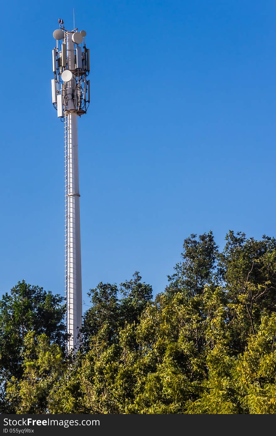 Telecommunication mast and green trees at the blue sky