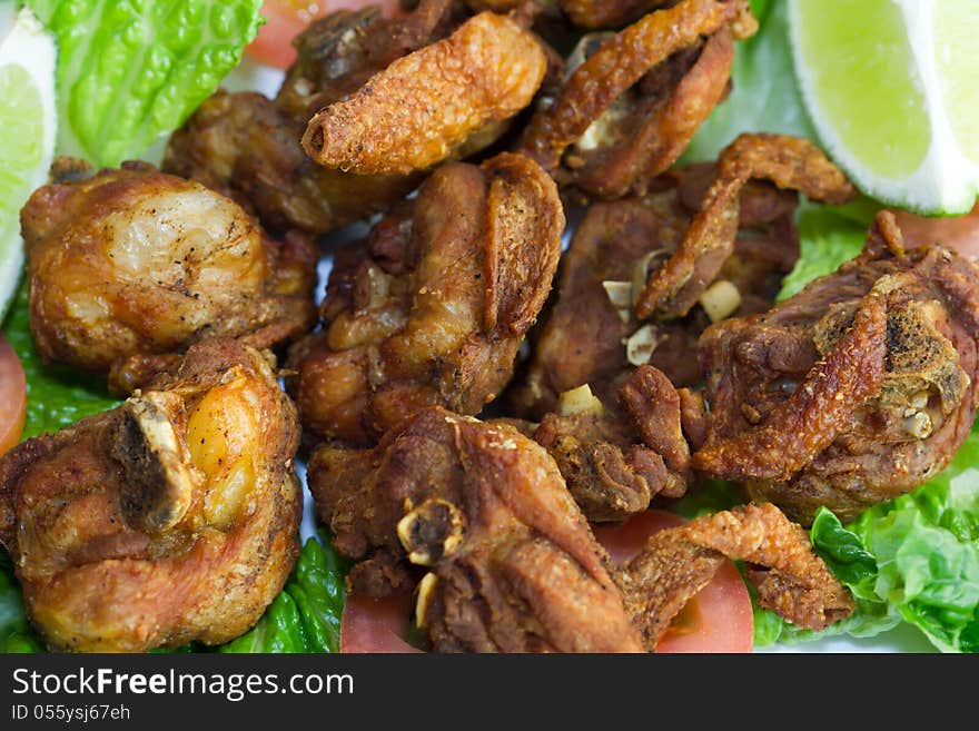 Fried chicken parts with bone on a bed of tomato and lettuce with a slice of lime.