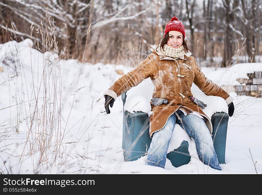 Young girl with red hat sitting on the arm-chair outside, outdoor portrait on a winter day