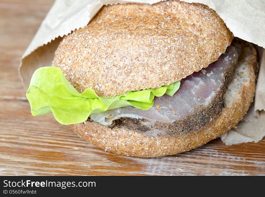 Fresh burger with paper wrapping on the rough wooden surface. Fresh burger with paper wrapping on the rough wooden surface