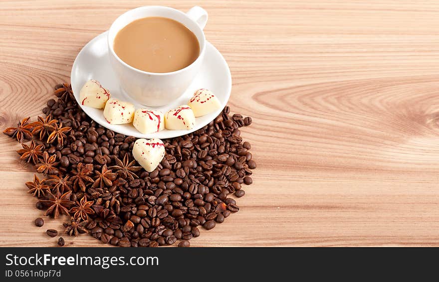 Cup of coffee with beans and white chocolate heart candy  over wooden background