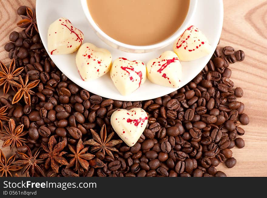 Cup of coffee with beans and white chocolate heart candy over wooden background.