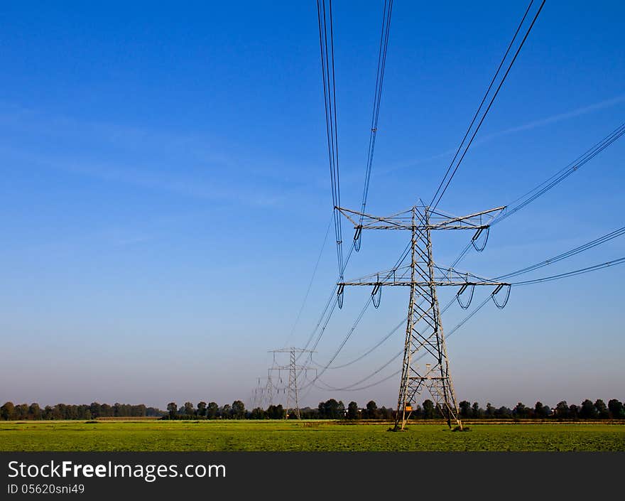 A lush field with electricity pylons and trees in background on a hot summers day. A lush field with electricity pylons and trees in background on a hot summers day.