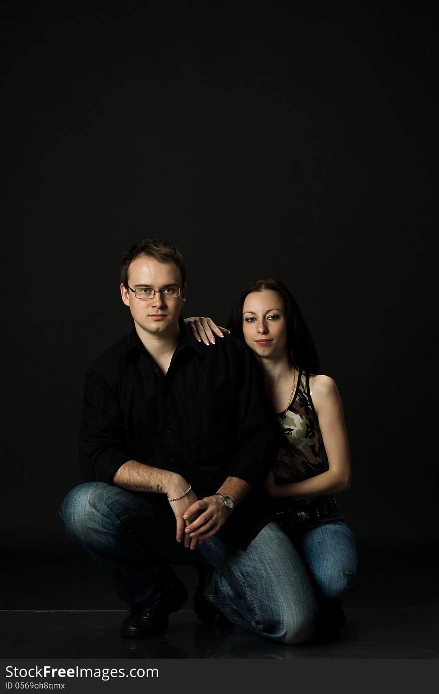 Handsome young couple posing sitting in studio on black background