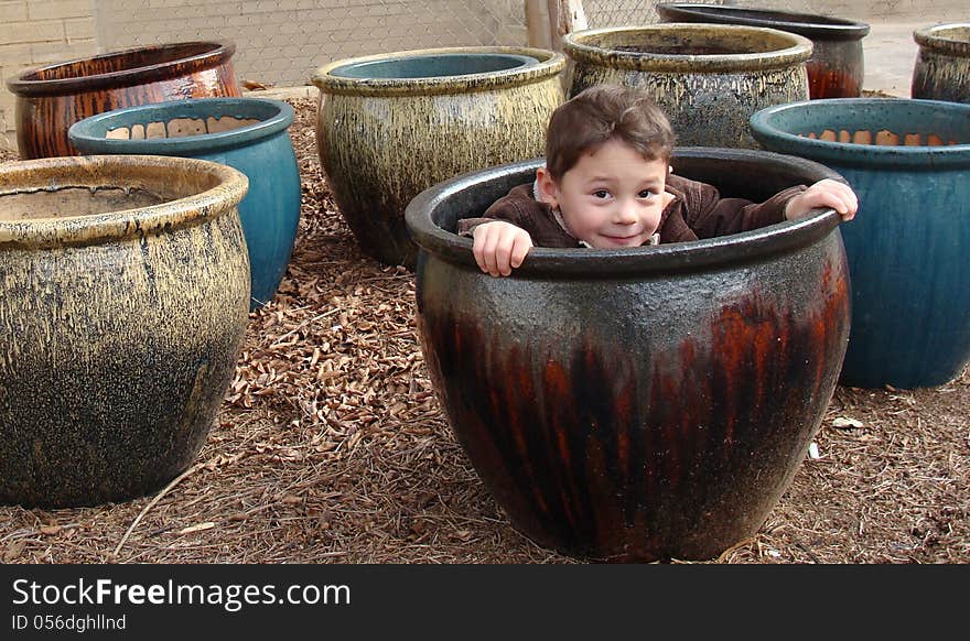 Little boy peeking out of the flower pot sitting in the midst of the pots. Little boy peeking out of the flower pot sitting in the midst of the pots