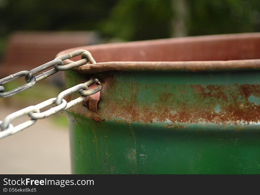 Image of a chained rusted garbage can in a park. Selective focus on where the chain is connected to the garbage can. Lots of space for content. Image of a chained rusted garbage can in a park. Selective focus on where the chain is connected to the garbage can. Lots of space for content.