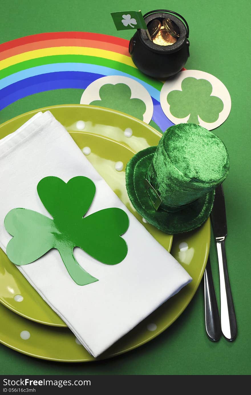 St Patrick's Day party table setting decorated with green polka dot plates, shamrocks, pot of gold and leprechaun hat with rainbow on green background. St Patrick's Day party table setting decorated with green polka dot plates, shamrocks, pot of gold and leprechaun hat with rainbow on green background.