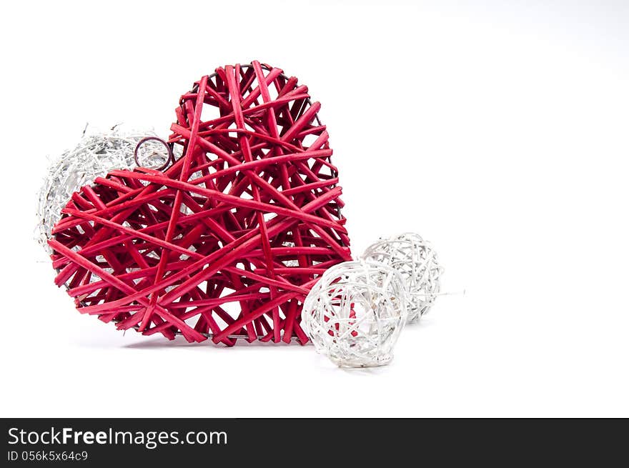Red wicker heart resting on small white wicker balls at an angle on white background
