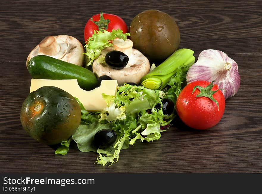 Arrangement of Red an Green Tomatoes, Lettuce, Leek, Raw Mushrooms, Black Olives, Cheese, Cucumber and Garlic closeup on Dark Wood background. Arrangement of Red an Green Tomatoes, Lettuce, Leek, Raw Mushrooms, Black Olives, Cheese, Cucumber and Garlic closeup on Dark Wood background