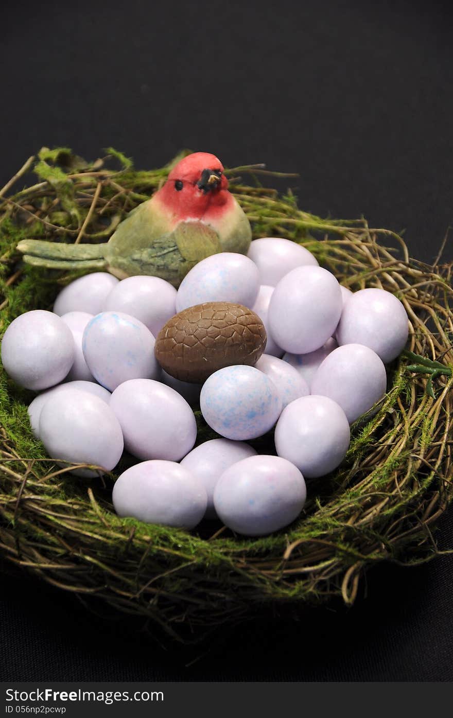 Close-up of chocolate Easter egg among sugar coated candy marble eggs in moss birds nest against a black background. Vertical portrait orientation. Close-up of chocolate Easter egg among sugar coated candy marble eggs in moss birds nest against a black background. Vertical portrait orientation.