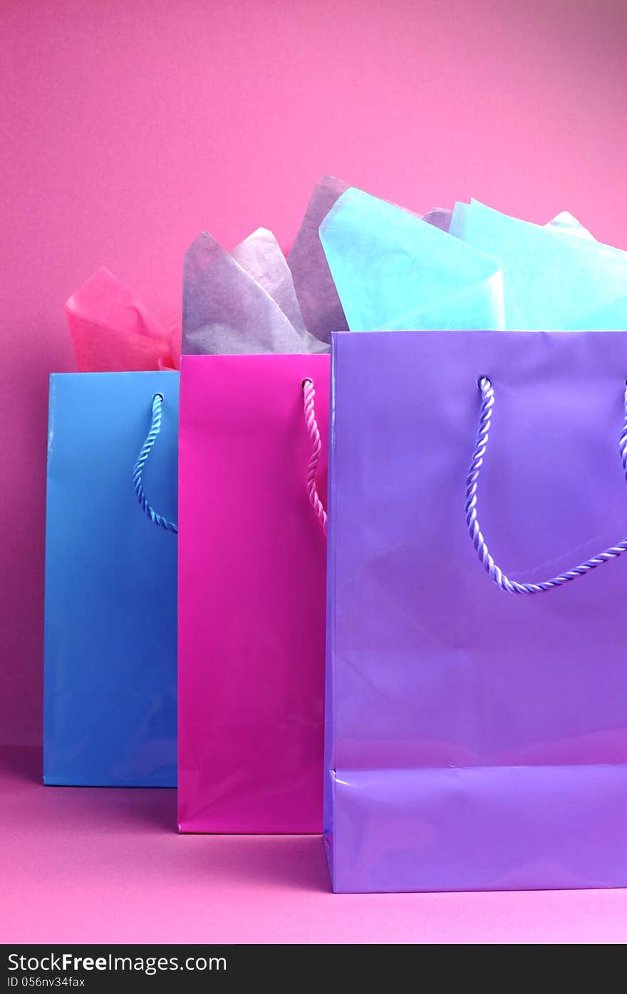 Retail therapy, I love shopping, concept with colorful pink, blue and purple shopping bags against a pink background, vertical side view. Retail therapy, I love shopping, concept with colorful pink, blue and purple shopping bags against a pink background, vertical side view.