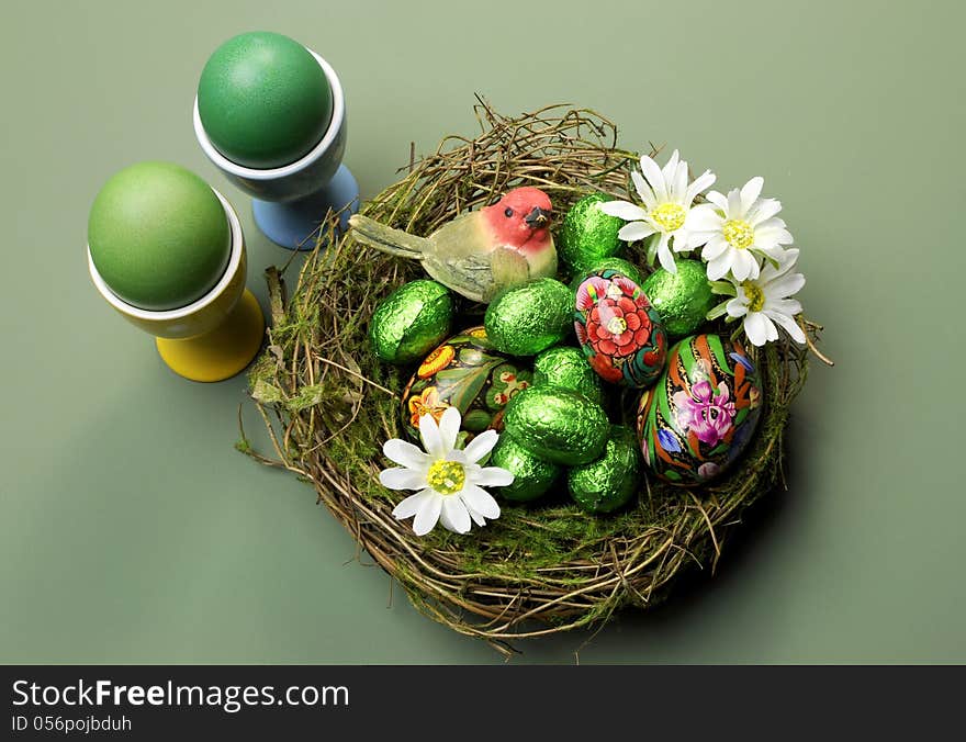 Happy Easter nest of chocolate and hand painted eggs, bird and daisies on a green table setting. Happy Easter nest of chocolate and hand painted eggs, bird and daisies on a green table setting.