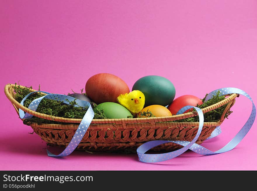 Rainbow color easter eggs on grass in wicker basket with blue polka dot ribbon against a pink background. Rainbow color easter eggs on grass in wicker basket with blue polka dot ribbon against a pink background.