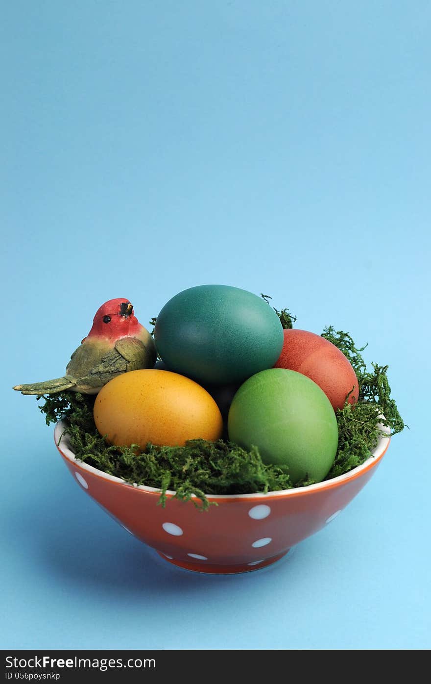 Bright and cheerful Happy Easter still life with rainbow color eggs in orange polka dot bowl against a blue background.