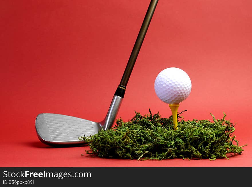 Sporting and Leisure pursuit, golf club iron, yellow tee with white golf ball on grass against  a red background, with copy space. Sporting and Leisure pursuit, golf club iron, yellow tee with white golf ball on grass against  a red background, with copy space.