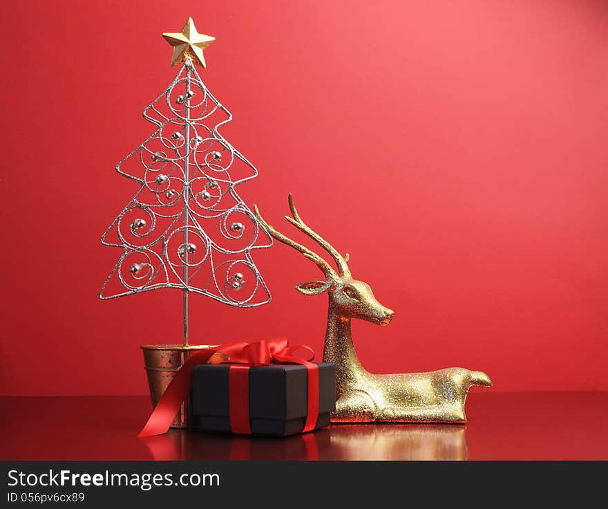 Silver and gold glitter Christmas tree and reindeer ornaments with black and red present gift still life against a festive holiday red background. Silver and gold glitter Christmas tree and reindeer ornaments with black and red present gift still life against a festive holiday red background.