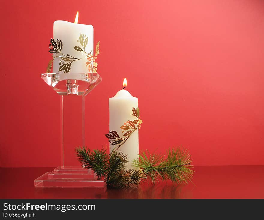 Lit white Christmas candles with festive holiday gold decoration and pine branches still life against a festive holiday red background.