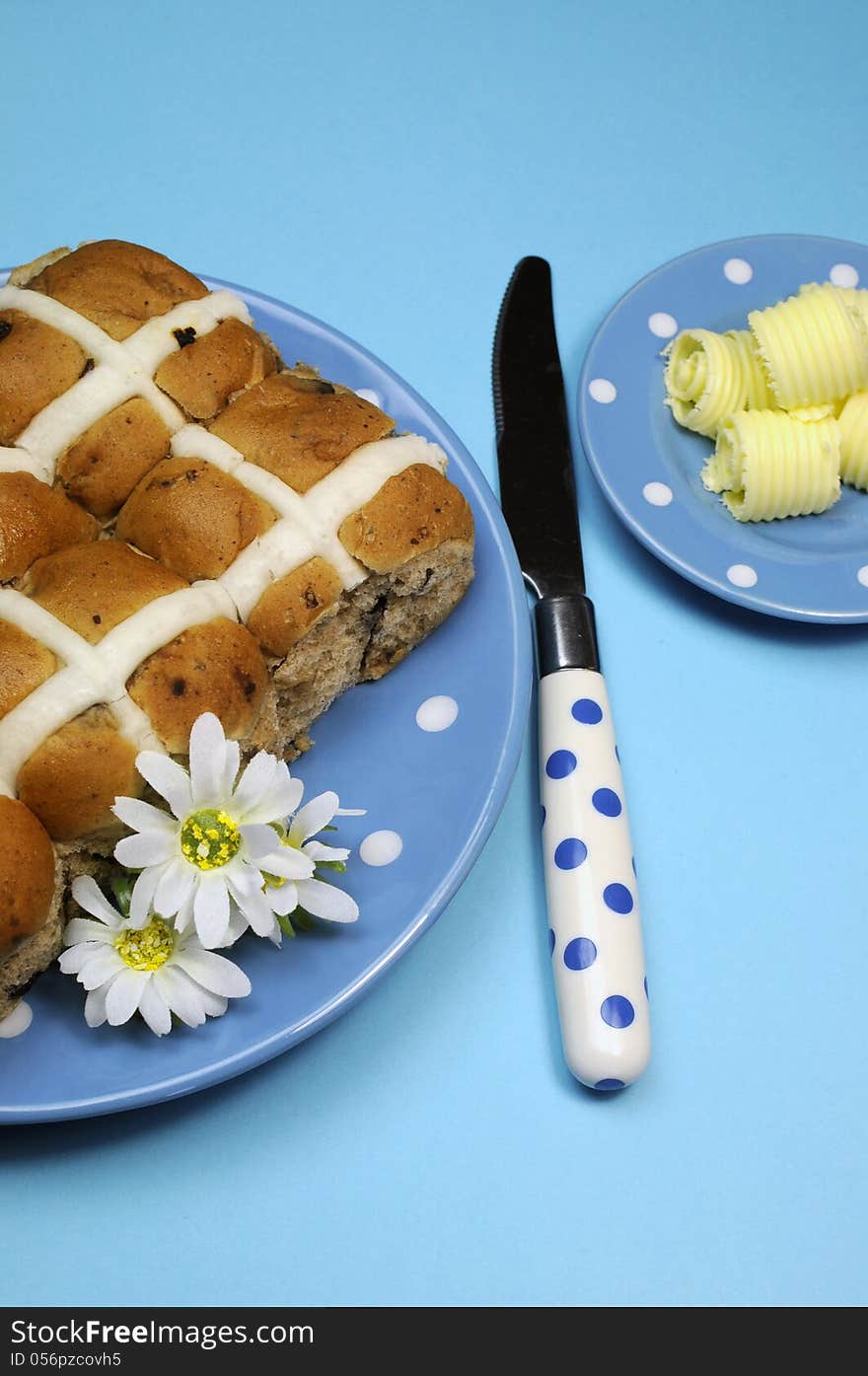 Traditional Australian and English Easter Good Friday meal, Hot Cross Buns, on blue polka dot plate with knife and butter curls on blue background. Traditional Australian and English Easter Good Friday meal, Hot Cross Buns, on blue polka dot plate with knife and butter curls on blue background.