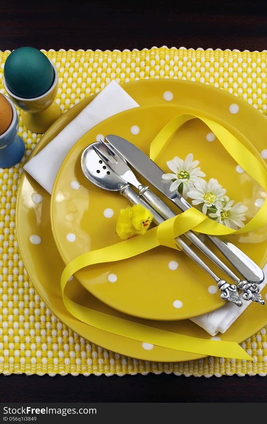 Yellow theme Easter dining table setting with eggs, chick and daisies. Vertical portrait orientation. Yellow theme Easter dining table setting with eggs, chick and daisies. Vertical portrait orientation.