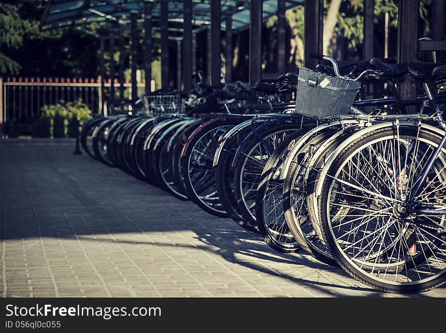 Many bicycles stand one-behind-one on the sidewalk