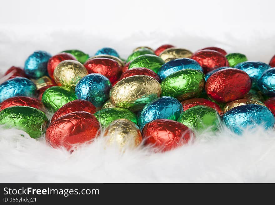 Chocolate easter eggs in colorful aluminium foil on white down. Chocolate easter eggs in colorful aluminium foil on white down