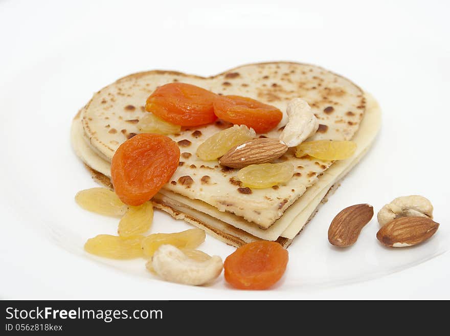 Heart-shaped pancake with dried apricots, almond, hazelnuts, cashew and raisins on white plate. Heart-shaped pancake with dried apricots, almond, hazelnuts, cashew and raisins on white plate