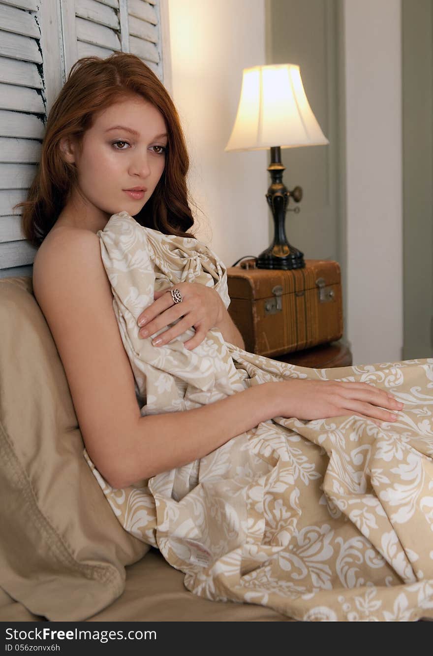 An image of a pretty young woman lying in bed under sheets. An image of a pretty young woman lying in bed under sheets