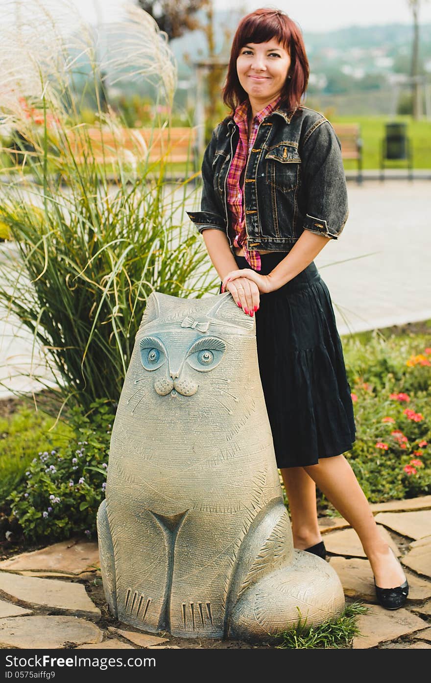 Young woman standing near funny cat statue in summer day