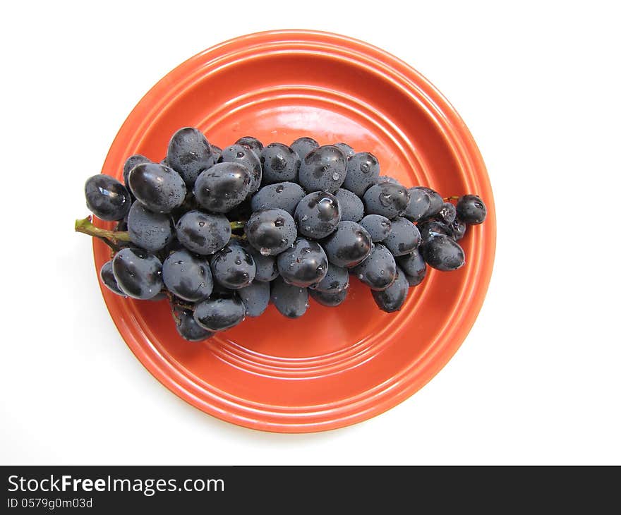 Ripe black grapes in orange ceramic plate isolated on white background