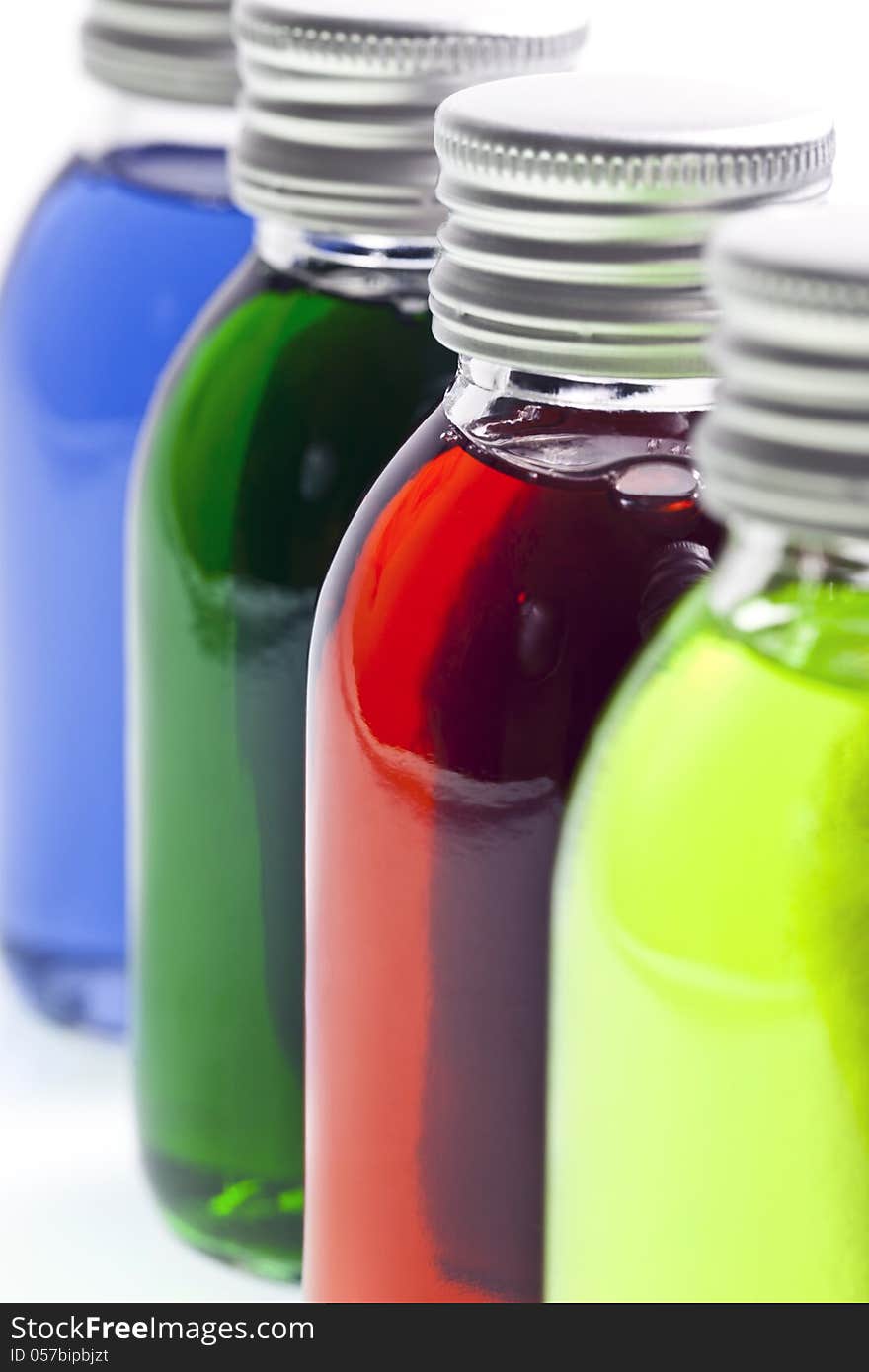 Bottles in a row with different colored liquid over white background. Bottles in a row with different colored liquid over white background