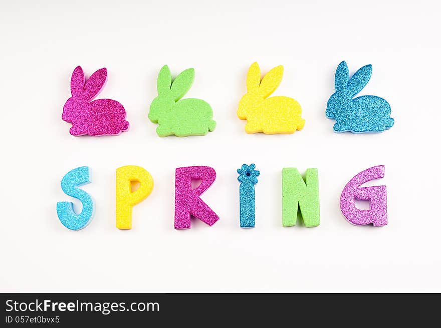 The word Spring in glitter colors of blue, yellow, purple, green. The letters are made of foam cutouts on white background. The word Spring in glitter colors of blue, yellow, purple, green. The letters are made of foam cutouts on white background.