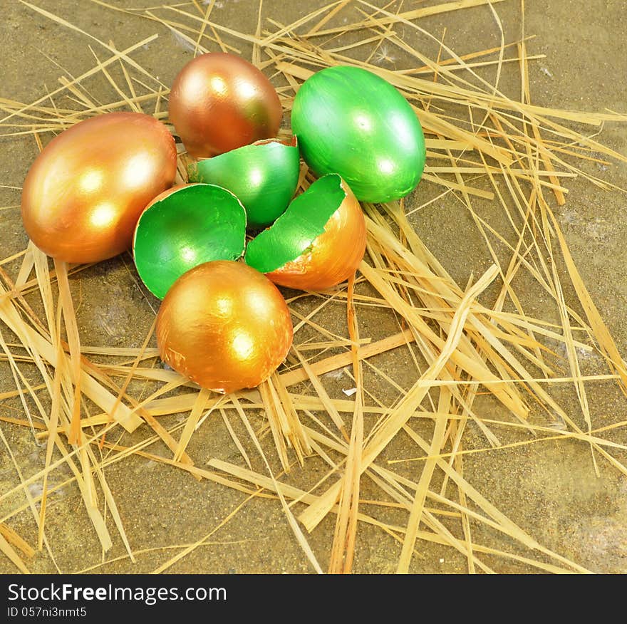 Gold Easter eggs with eggshell and straw on the sand background. Gold Easter eggs with eggshell and straw on the sand background