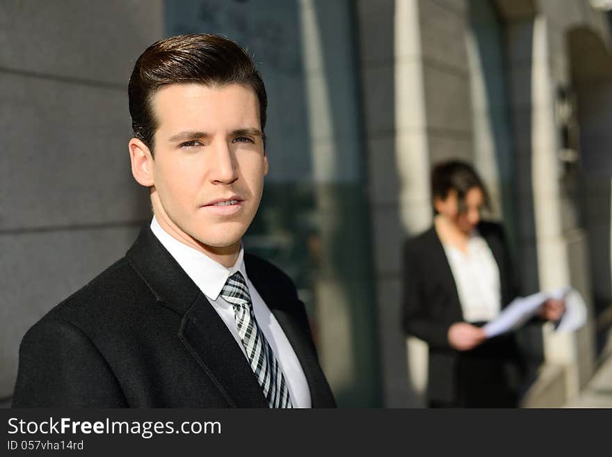 Portrait of attractive young businessman in the city with beautiful businesswoman in the background. Portrait of attractive young businessman in the city with beautiful businesswoman in the background