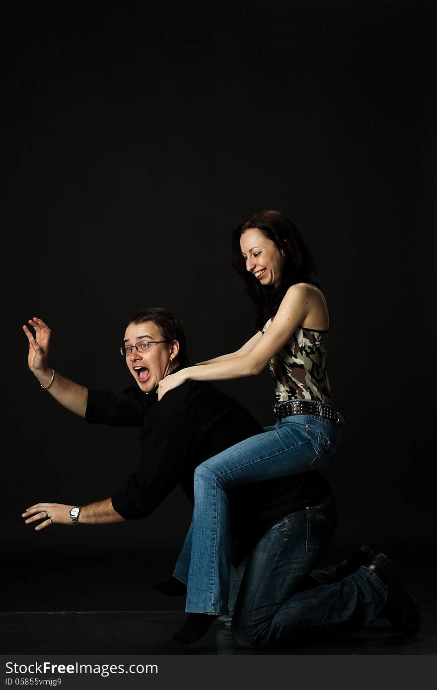 Funny young couple play in studio on black background