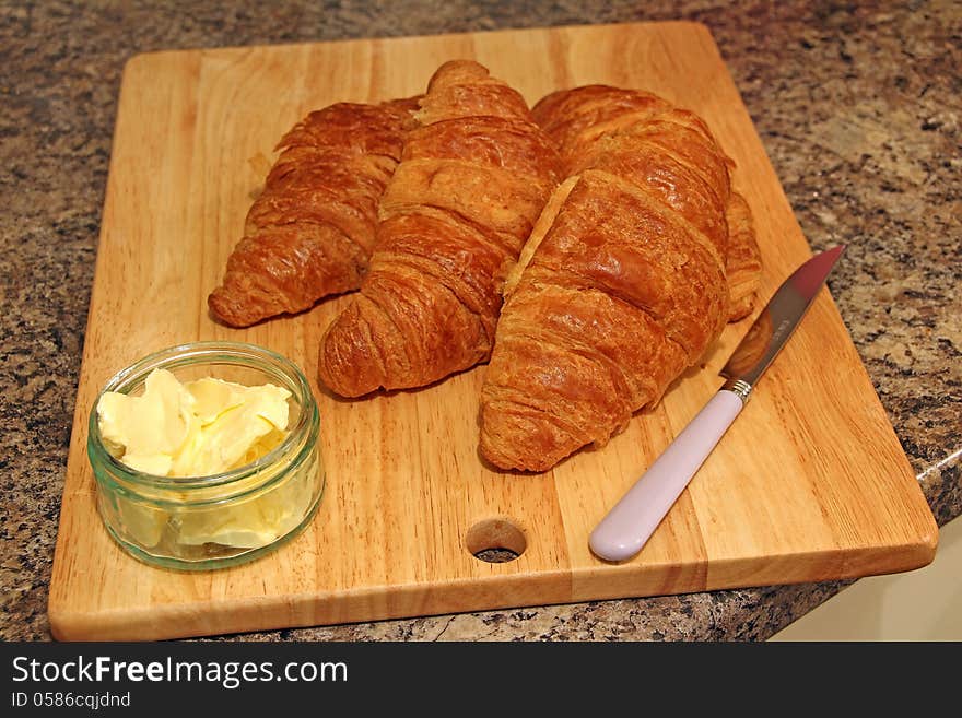 Photo showing delicious croissants on board with butter and knife. Photo showing delicious croissants on board with butter and knife.