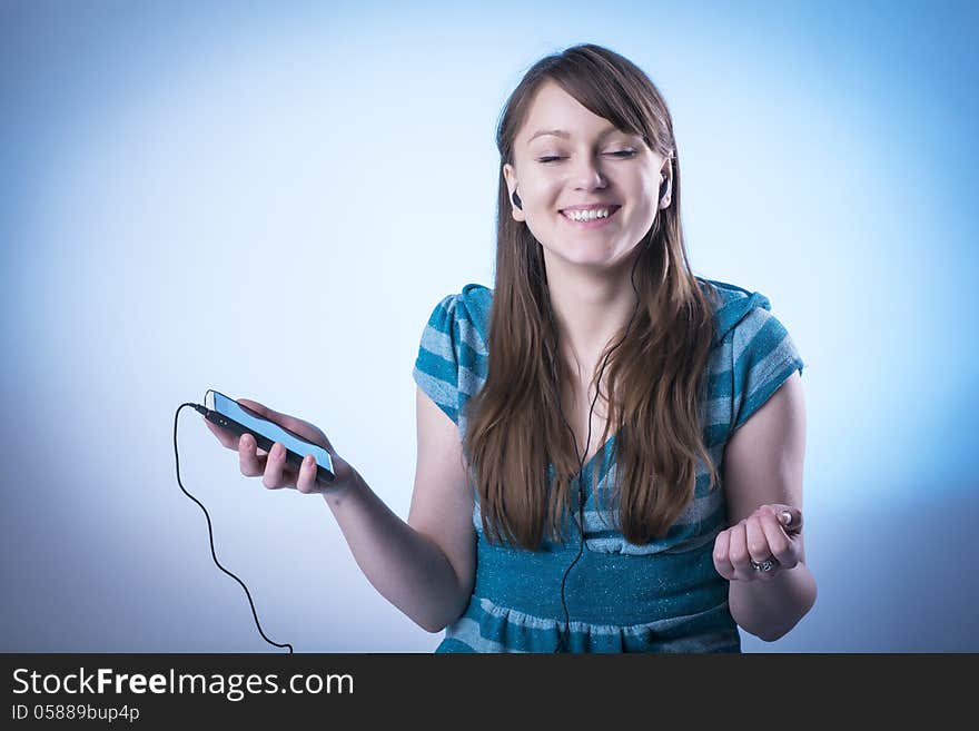 Cute young female hearing music from an mp3 player, isolated on light blue. Cute young female hearing music from an mp3 player, isolated on light blue