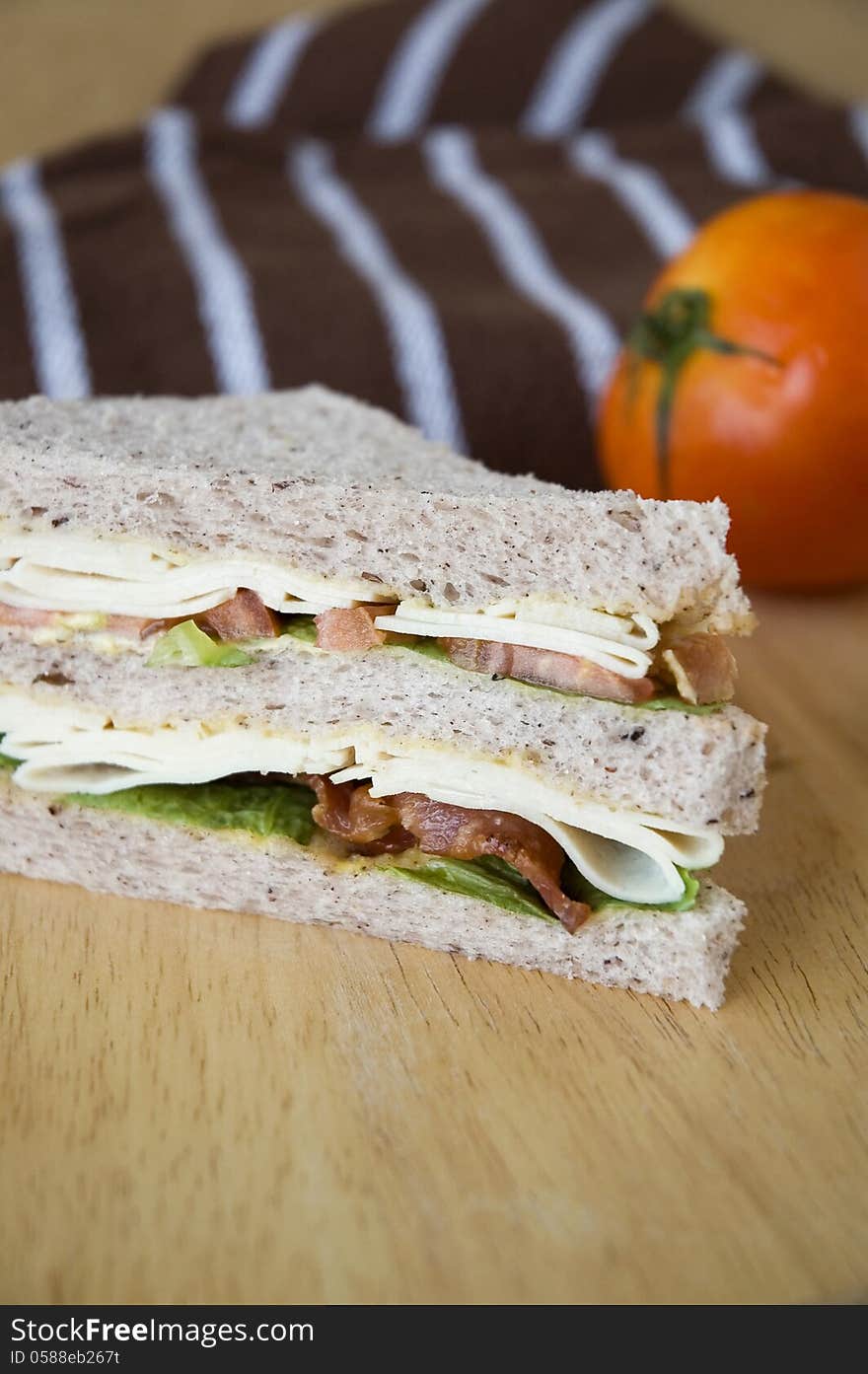 Close up bacon and chicken sandwich on wooden table with tomato background. Close up bacon and chicken sandwich on wooden table with tomato background