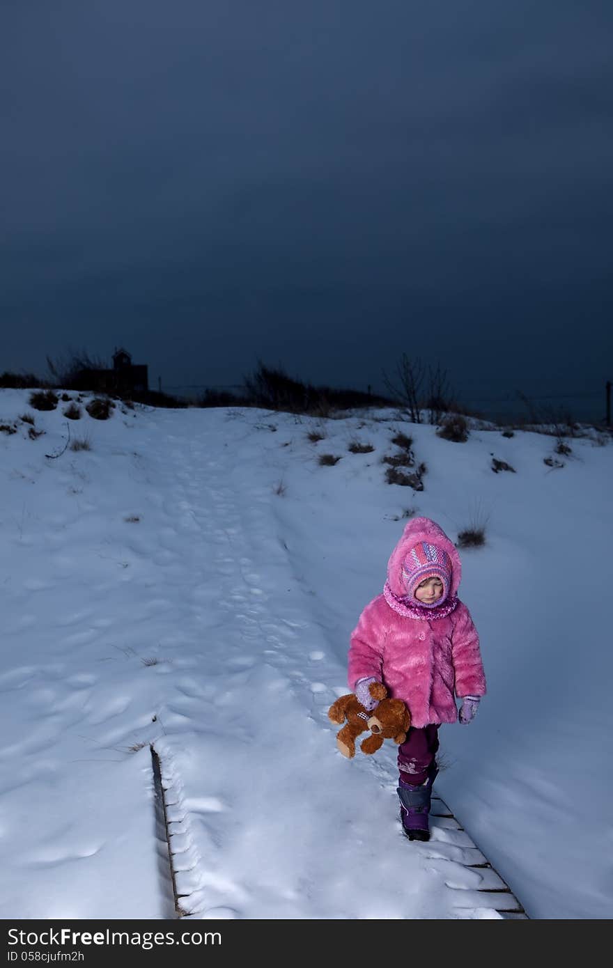 Sad girl walking away on winter path with teddy bear in her hands