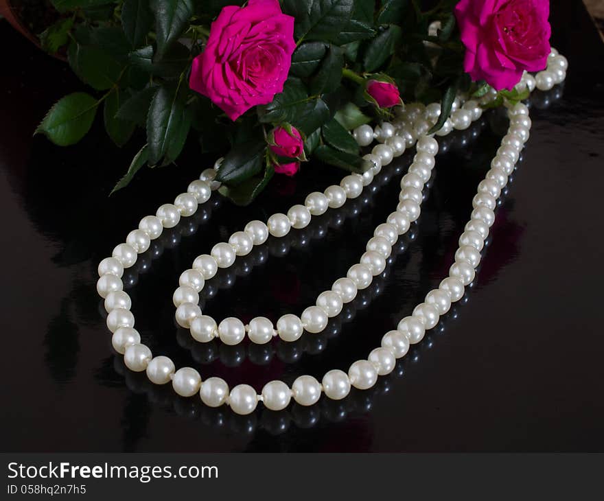 Pearl necklace and bouquet of roses on a black background