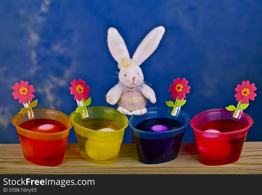 Painted eggs in containers , rabbit and flowers on a blue background. Painted eggs in containers , rabbit and flowers on a blue background.