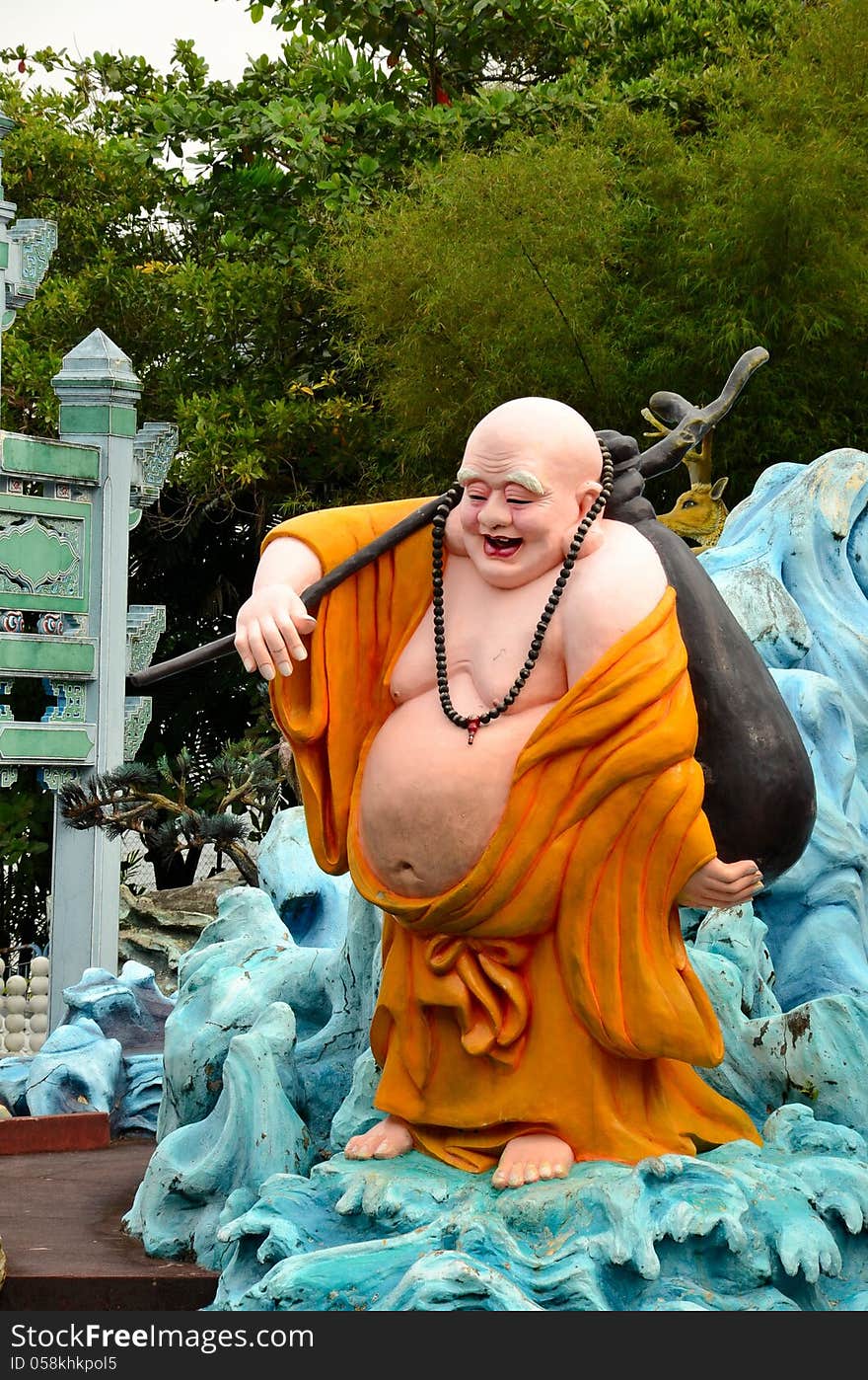 A saffron robed fat laughing Buddhist monk carrying stick and satchel on his travels. Haw Par Villas park, Singapore. A saffron robed fat laughing Buddhist monk carrying stick and satchel on his travels. Haw Par Villas park, Singapore.