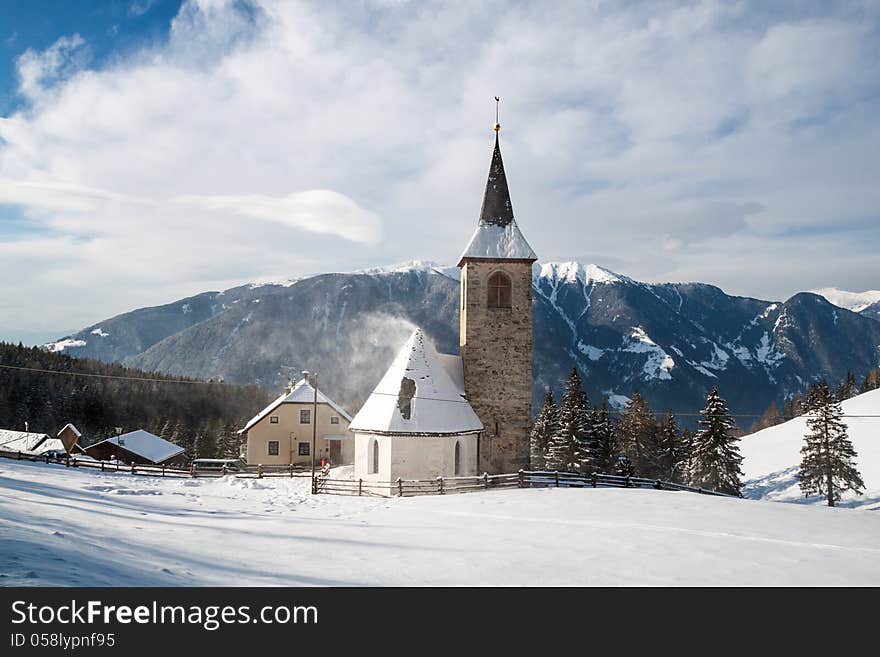 A wintertime view of a small church with a tall steeple in Montassilone, Sud Tyrol