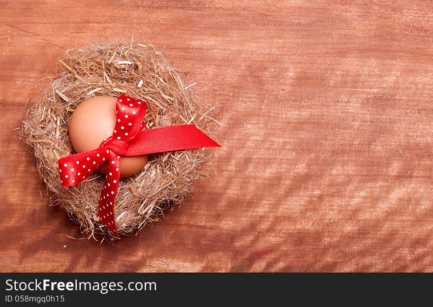 Egg swollen by a red bow lies in the nest on the wooden background