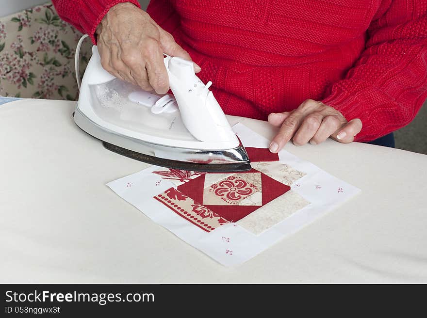 A woman irons a piece of fabric for use in a quilt. A woman irons a piece of fabric for use in a quilt.